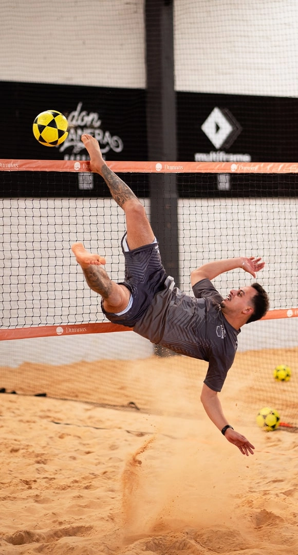 Homem saltando para alcanar bola com os ps durante partida de futevlei.