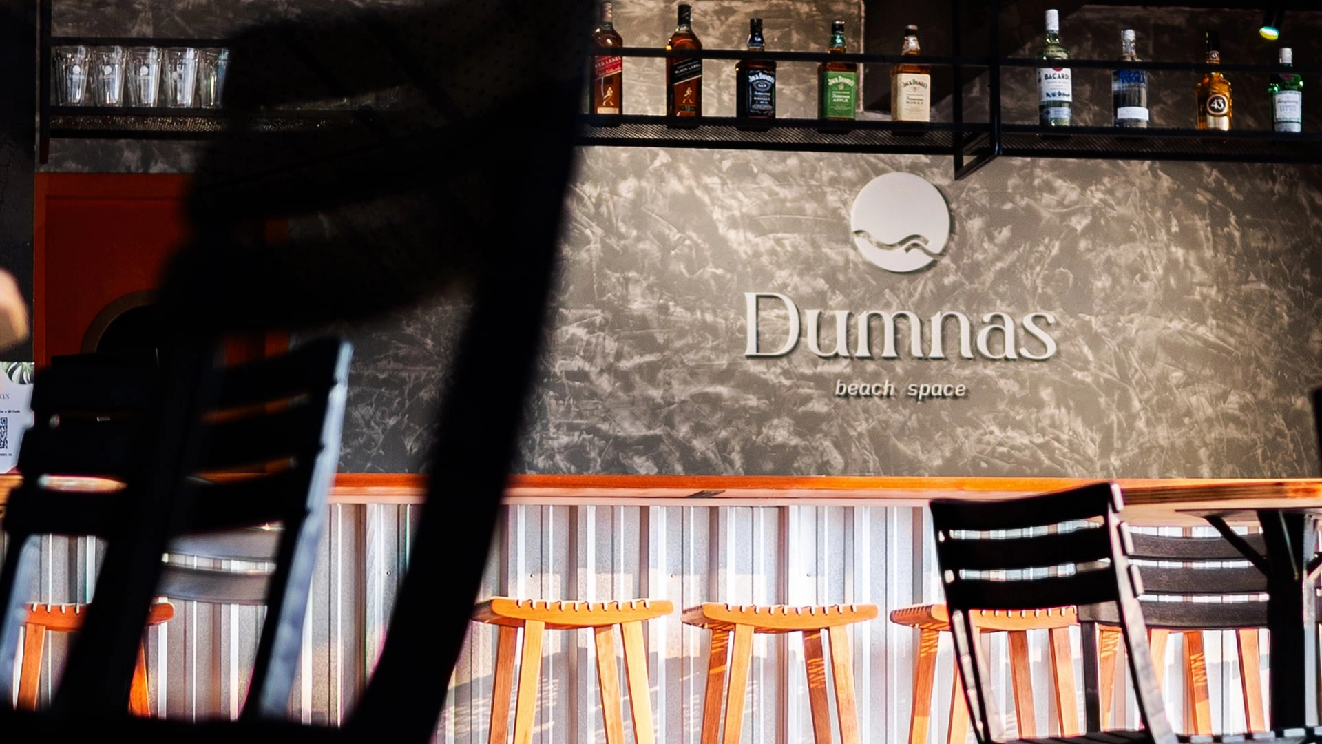 O melhor bar e conveniência Bar do Dumnas - diversas cadeiras e mesas e à frente do bar, banquetas.