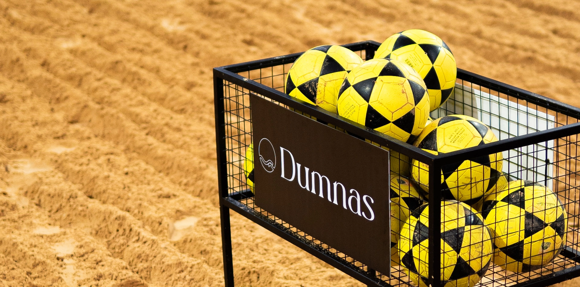 4 quadras de areia cobertas Bolas de futevôlei em cesto com logo do Dumnas.